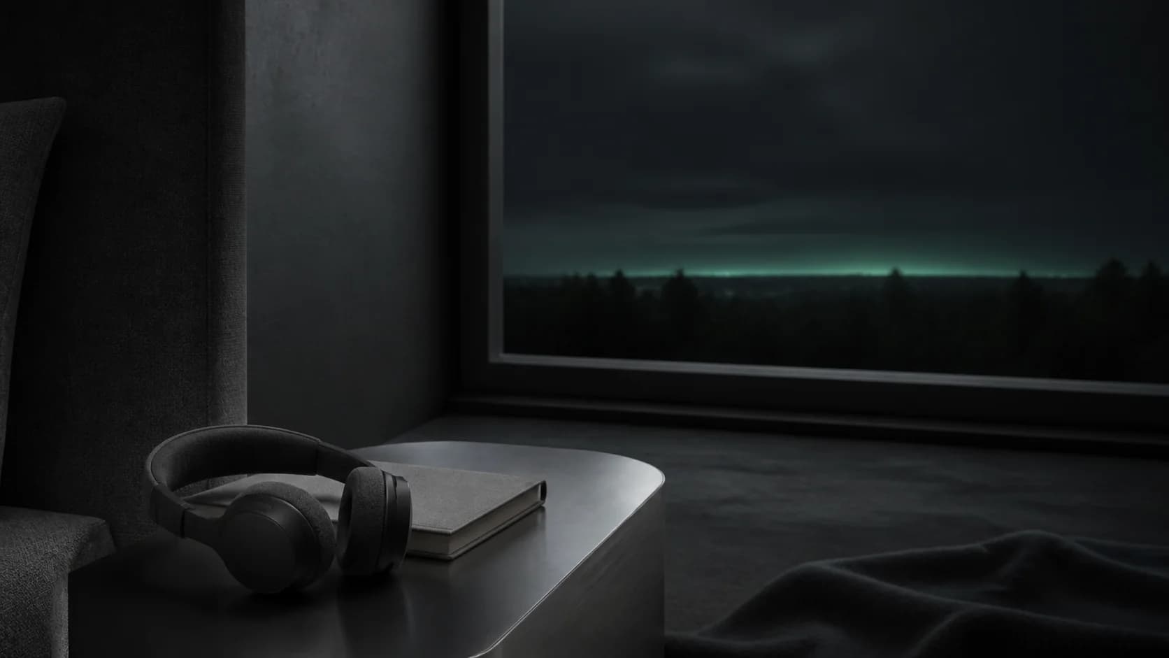 Graphite headphones and a notebook beside a window at night